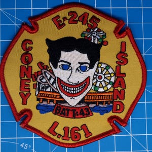 May include: Embroidered patch with a yellow background and red trim. The patch features the Coney Island Joker face, roller coaster, and Ferris wheel. Text includes "CONEY ISLAND", "E-245", "BATT:43", and "L.161".