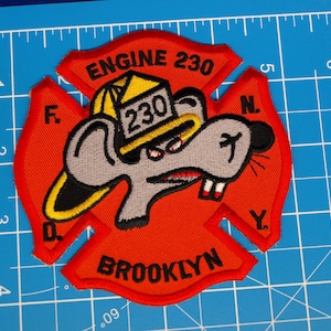 May include: A red embroidered patch shaped like a Maltese cross featuring a cartoon mouse wearing a yellow firefighter helmet labeled 230. The patch includes the text ENGINE 230, F.D.N.Y., and BROOKLYN, measuring approximately 4 inches tall.