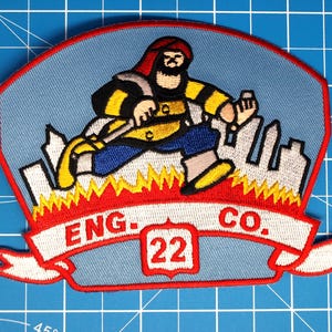 May include: Embroidered patch featuring a firefighter running through flames, with a cityscape silhouette in the background. The patch has a light blue background with a red border and a white banner that reads "ENG. CO. 22".