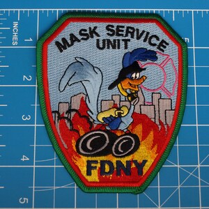 May include: Embroidered patch featuring a cartoon Road Runner character with a firefighter theme. The patch reads "MASK SERVICE UNIT" and "FDNY" in bold letters. The design includes flames, city buildings, and a fire department emblem.