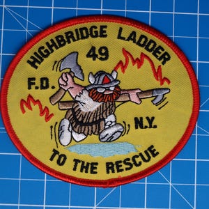 Puede incluir: Un parche redondo con un centro amarillo y un borde rojo. El parche presenta un bombero vikingo de dibujos animados sosteniendo hachas, con el texto "HIGHBRIDGE LADDER 49 F.D. N.Y. TO THE RESCUE".