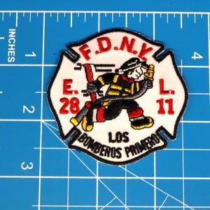 May include: Embroidered patch featuring a firefighter in action, holding a hose. The patch is white with red and black accents, and the text "F.D.N.Y. E. 28 L. 11 LOS BOMBEROS PRIMERO" is displayed. The patch measures approximately 3 inches in height.