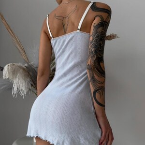 Puede incluir: Un vestido lencero azul claro con tirantes blancos y un dobladillo festoneado. El vestido tiene un sutil estampado floral y una textura acanalada. Las correas son ajustables. El vestido es de largo mini.