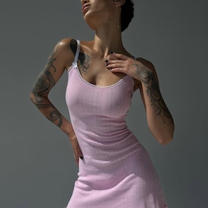 Puede incluir: Vestido lencero rosa claro de punto acanalado con ribete y tirantes blancos. El vestido tiene un dobladillo festoneado y una silueta ajustada. La modelo lleva el vestido. El fondo es gris liso.