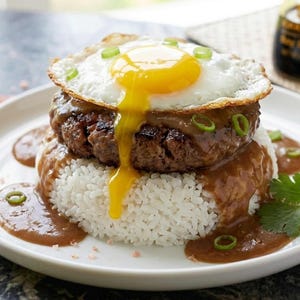 May include: A plate of Hawaiian-style loco moco. It features a hamburger patty, white rice, gravy, and a fried egg with a runny yolk. Garnished with green onions and parsley.