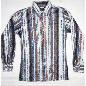May include: A long-sleeve button-down shirt featuring a vertical striped pattern in shades of light blue, dark brown, and black. The shirt has a pointed collar, a front button placket with white buttons, and buttoned cuffs on each long sleeve.