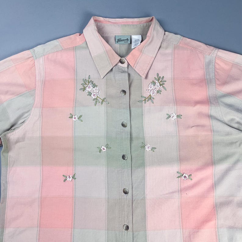 May include: A pink and green plaid button-down shirt with embroidered flowers. The shirt has a collar and long sleeves.