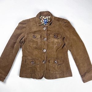 May include: A brown corduroy jacket with four front pockets and button fastenings. The jacket features a collared neckline and a patterned lining visible at the collar. The brand tag "GAP" is visible on the inside of the collar.
