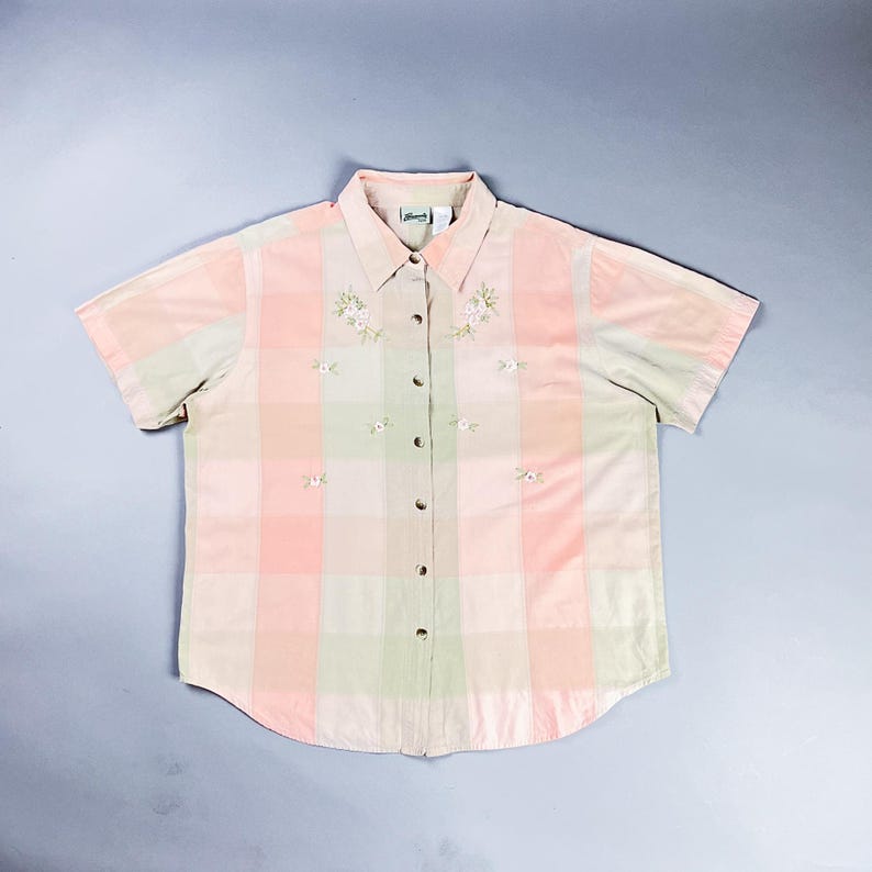 May include: A pink and green plaid short-sleeved button-down shirt with embroidered flowers.
