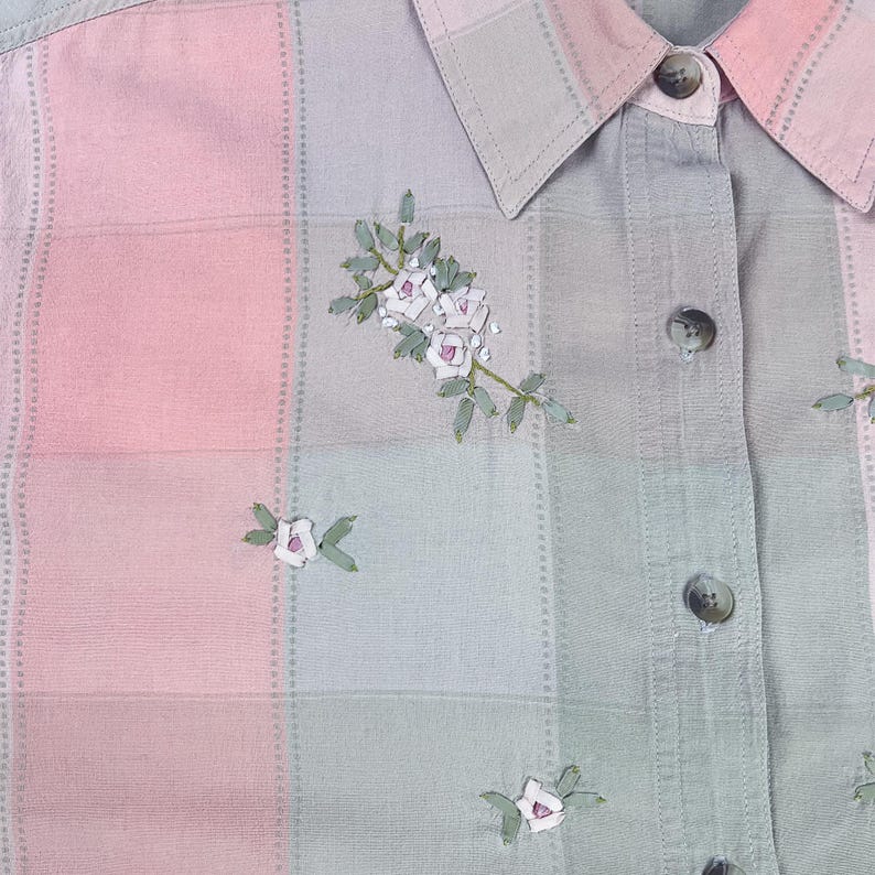 May include: A light pink and green plaid shirt with embroidered white flowers. The shirt has a button-up collar and long sleeves.