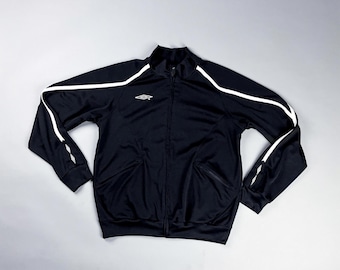 Puede incluir: Chaqueta deportiva negra con rayas blancas en las mangas y los hombros. Tiene una cremallera completa y dos bolsillos delanteros. Un pequeño logotipo está presente en el pecho.
