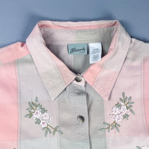 May include: A pink and grey plaid button-up shirt with embroidered flowers. The shirt has a collar and a label that reads "Pennant Plus".