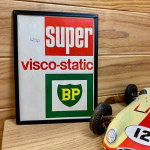 May include: Framed vintage sign with the words "SUPER visco-static" in red and white. The sign also features a green square with a yellow "BP" logo. A toy race car with the number 12 is in the foreground.
