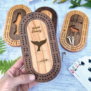 Peut inclure: Planches de cribbage en bois avec des motifs grav&eacute;s. L'une repr&eacute;sente une queue de baleine, une autre un loup et une troisi&egrave;me un &eacute;lan. La planche centrale est personnalis&eacute;e avec "Smith Family". Comprend des chevilles et des cartes &agrave; jouer.
