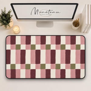 May include: A rectangular desk mat featuring a repeating geometric pattern of vertical stripes and small squares in shades of burgundy, dusty pink, cream, and olive green. The design has a textured, painted appearance with a black border.