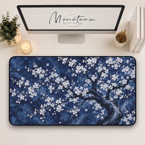 May include: A rectangular desk mat featuring a dark blue background with a detailed illustration of a flowering tree with white blossoms. The design includes swirling patterns and a textured appearance, providing a wide surface for computer peripherals.