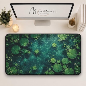 May include: A rectangular desk mat featuring a high-resolution print of a dark green pond surface covered in lily pads and aquatic foliage. The mat has a black border and is positioned on a white desk surface below a computer monitor displaying the text Moneteau Unique Designs.