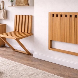 Puede incluir: Se muestra una silla plegable de madera y una silla plegable a juego montada en la pared. Las sillas son de madera de color claro y tienen un diseño de listones. La silla montada en la pared está plegada contra una pared blanca.