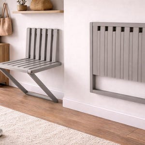 May include: A grey wall-mounted folding chair featuring a slatted design. The chair is shown in two positions: one fully extended as a seat with a backrest and angled legs, and another folded flat against the wall as a rectangular panel.