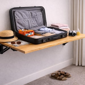 Könnte beinhalten: Ein schwarzer Koffer, teilweise geöffnet, gefüllt mit Kleidung und Reiseutensilien, steht auf einem hölzernen Klapptisch. Ein Strohhut, eine Sonnenbrille und eine Karte liegen auf dem Tisch. Eine Kamera und Sandalen sind ebenfalls zu sehen.