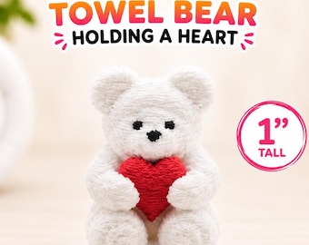 May include: A white mini towel bear holding a red heart, featuring the text Mini TOWEL BEAR HOLDING A HEART and a circular graphic indicating 1 inch tall. The bear has black embroidered eyes and a nose, crafted from textured white fabric.