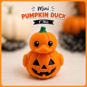 May include: A small orange duck-shaped figure with a pumpkin-like body and a green stem on its head. The front features a carved jack-o'-lantern face with black triangular eyes and a jagged mouth. Text above reads Mini PUMPKIN DUCK 1" TALL.