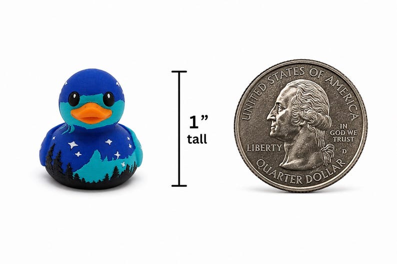 May include: A small blue rubber duck featuring a night sky design with white stars and a black forest silhouette at the base. The duck has an orange beak and is shown next to a United States quarter dollar coin, indicating a height of 1 inch.