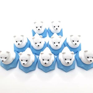 May include: A collection of eleven small, white polar bear figurines, each mounted on a light blue, faceted hexagonal base. The bears have black eyes and noses, and are arranged in a triangular formation against a plain white background.