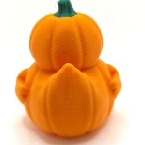 May include: A small, orange, 3D-printed figurine shaped like a duck with a pumpkin-like body. The figure features a rounded, ribbed orange base and a smaller, rounded orange head section, topped with a small, textured green stem.