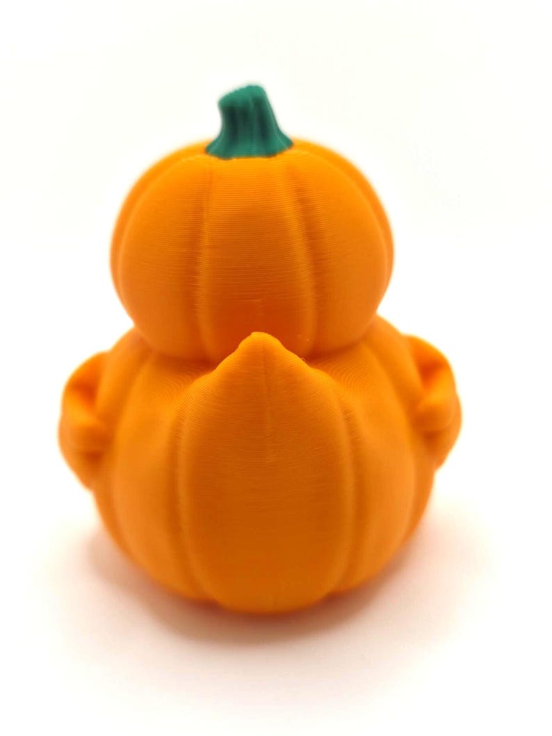 May include: A small, orange, 3D-printed figurine shaped like a duck with a pumpkin-like body. The figure features a rounded, ribbed orange base and a smaller, rounded orange head section, topped with a small, textured green stem.