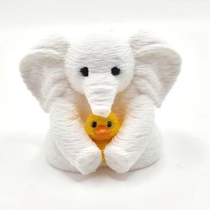 Mini towel animal elephant holding a yellow duck, 3D printed collectible by Florida Cruise Ducks. White elephant design with textured towel-like appearance, approximately 1 inch tall. Shown from multiple angles including front, side, back, hand-held size comparison, and marker comparison. Perfect for cruise duck hiding, cruise gifts, duck exchanges, party favors, and miniature collectibles. Exclusive Florida Cruise Ducks design.