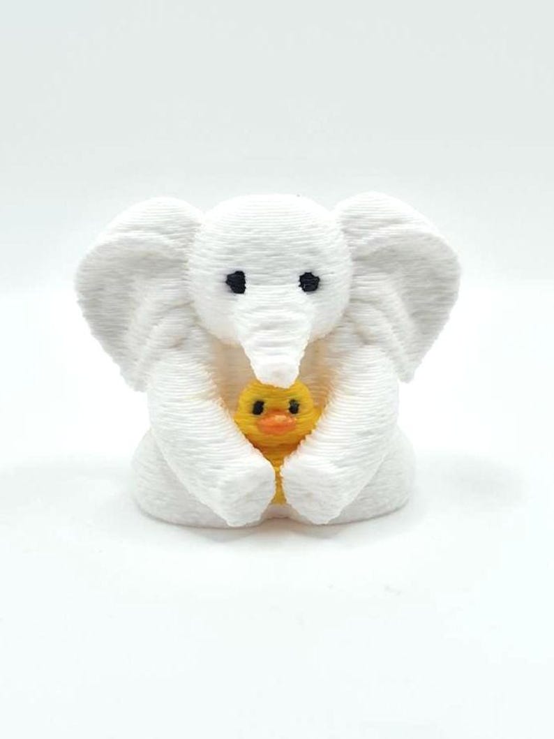 Mini towel animal elephant holding a yellow duck, 3D printed collectible by Florida Cruise Ducks. White elephant design with textured towel-like appearance, approximately 1 inch tall. Shown from multiple angles including front, side, back, hand-held size comparison, and marker comparison. Perfect for cruise duck hiding, cruise gifts, duck exchanges, party favors, and miniature collectibles. Exclusive Florida Cruise Ducks design.