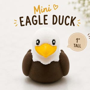Puede incluir: Una peque&ntilde;a figura con forma de pato y rasgos de &aacute;guila calva, con cabeza blanca, pico amarillo brillante y cuerpo marr&oacute;n oscuro. El texto superior dice Mini EAGLE DUCK y un globo de texto a la derecha indica 1" TALL.