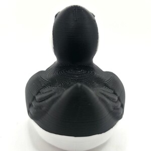 May include: A 3D printed duck figurine featuring a matte black head, neck, and back with visible horizontal layer lines. The lower portion of the duck is solid white, creating a distinct two-tone color scheme with a smooth, rounded base.