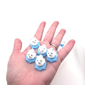 May include: A collection of small, white polar bear figurines, each perched atop a light blue, geometric, hexagonal base. The bears have simple black eyes and noses, and they are arranged in a cluster, showcasing their smooth, matte texture.