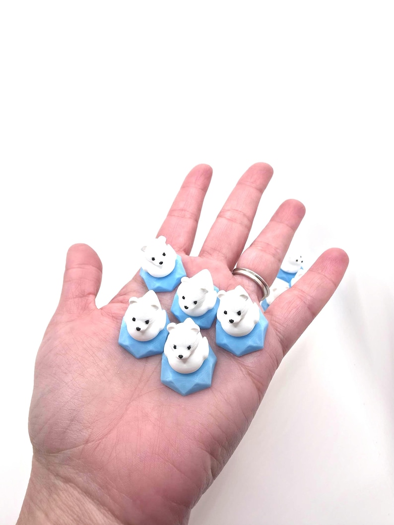 May include: A collection of small, white polar bear figurines, each perched atop a light blue, geometric, hexagonal base. The bears have simple black eyes and noses, and they are arranged in a cluster, showcasing their smooth, matte texture.