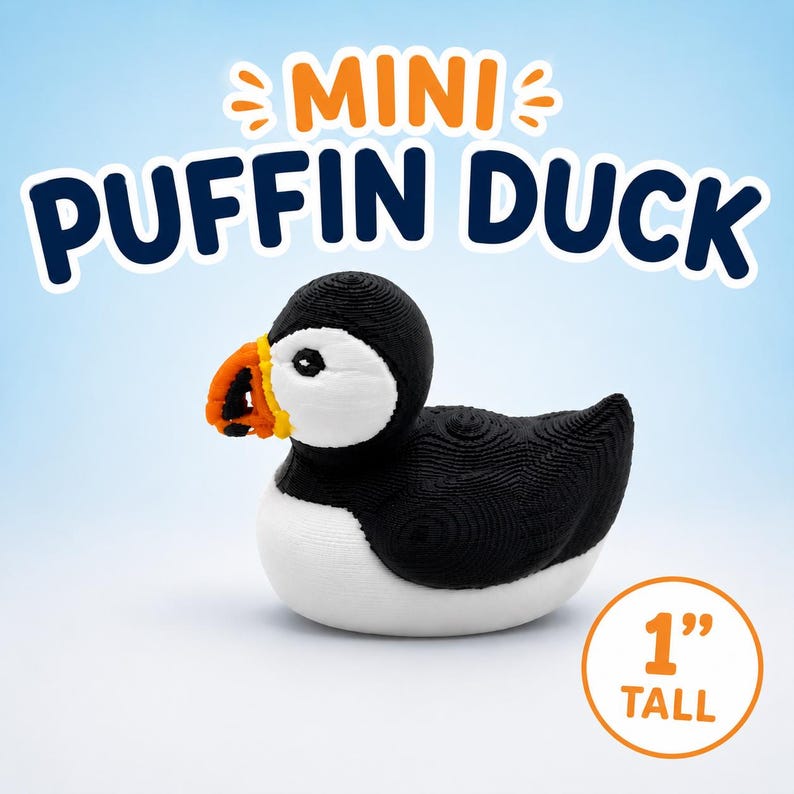 Puede incluir: Una peque&ntilde;a figura de pato frailecillo con cabeza, espalda y alas negras, cara y pecho blancos, y un pico naranja brillante. El texto MINI PUFFIN DUCK aparece arriba y una insignia circular indica que el art&iacute;culo mide 1 pulgada de alto.