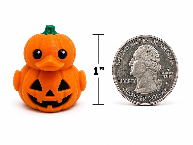 May include: An orange pumpkin-shaped rubber duck with a green stem on top, black eyes, and a carved jack-o'-lantern face on the body. A vertical line with the text 1 inch indicates the height next to a silver United States quarter dollar coin.