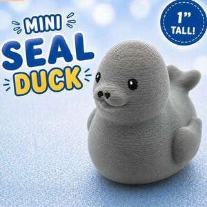 Puede incluir: Una figura gris impresa en 3D con forma de foca y rasgos de pato, que mide 2,54 cm de altura. La figura tiene una superficie texturizada, ojos negros peque&ntilde;os y una nariz. El texto en la imagen dice MINI SEAL DUCK y 1 TALL.
