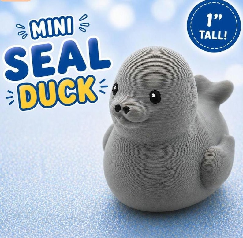 Puede incluir: Una figura gris impresa en 3D con forma de foca y rasgos de pato, que mide 2,54 cm de altura. La figura tiene una superficie texturizada, ojos negros peque&ntilde;os y una nariz. El texto en la imagen dice MINI SEAL DUCK y 1 TALL.
