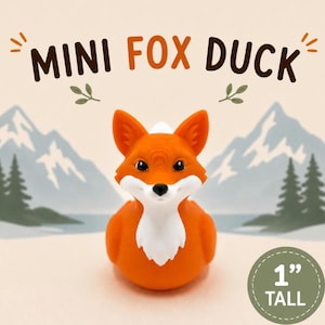 Puede incluir: Una peque&ntilde;a figura de pato de goma con forma de zorro naranja y blanco con ojos y nariz negros. El texto MINI FOX DUCK est&aacute; impreso sobre la figura, y una insignia circular indica que mide 2,54 cm de altura. El fondo muestra monta&ntilde;as.
