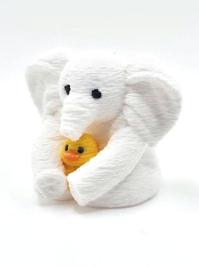 Mini towel animal elephant holding a yellow duck, 3D printed collectible by Florida Cruise Ducks. White elephant design with textured towel-like appearance, approximately 1 inch tall. Shown from multiple angles including front, side, back, hand-held size comparison, and marker comparison. Perfect for cruise duck hiding, cruise gifts, duck exchanges, party favors, and miniature collectibles. Exclusive Florida Cruise Ducks design.