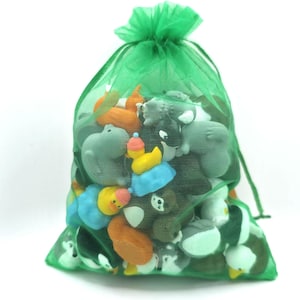 Puede incluir: Una bolsa de organza verde transl&uacute;cida con cord&oacute;n, llena de una colecci&oacute;n de peque&ntilde;as gomas de borrar de colores con formas de animales. Las figuras visibles incluyen patos amarillos, un oso pardo, un lobo gris y otras criaturas.