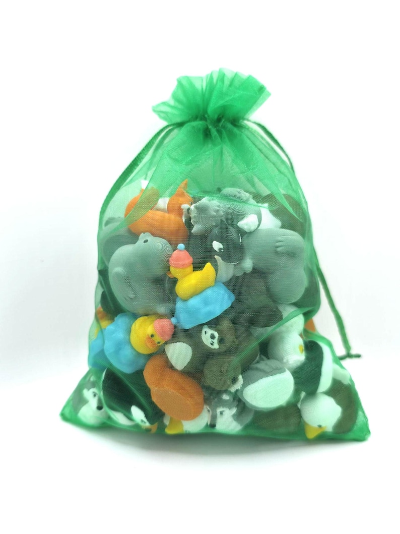 Puede incluir: Una bolsa de organza verde transl&uacute;cida con cord&oacute;n, llena de una colecci&oacute;n de peque&ntilde;as gomas de borrar de colores con formas de animales. Las figuras visibles incluyen patos amarillos, un oso pardo, un lobo gris y otras criaturas.