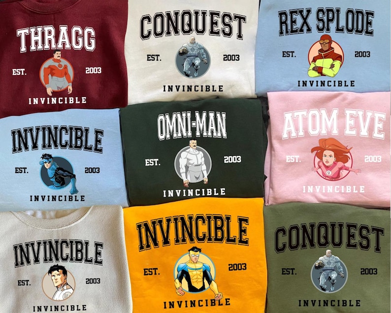 Puede incluir: Una colecci&oacute;n de sudaderas de cuello redondo en varios colores, cada una con un personaje diferente de la serie de c&oacute;mics Invincible. Las sudaderas muestran nombres de personajes, la palabra "Invincible" y el a&ntilde;o "2003". Cada dise&ntilde;o incluye una ilustraci&oacute;n circular del personaje.