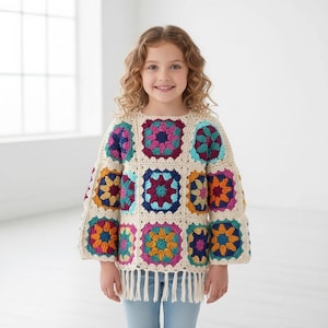 May include: A long-sleeved crochet sweater featuring a colorful granny square pattern in shades of magenta, teal, yellow, and orange, joined by cream-colored yarn. The garment has a round neckline and a straight hem finished with long cream fringe.