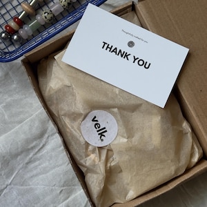 Pu&ograve; includere: Un cestino blu in filo metallico contiene due cucchiai da portata in acciaio inossidabile con manici decorativi. Una scatola di cartone contiene una carta con la scritta "THANK YOU" e un adesivo con la parola "velk."