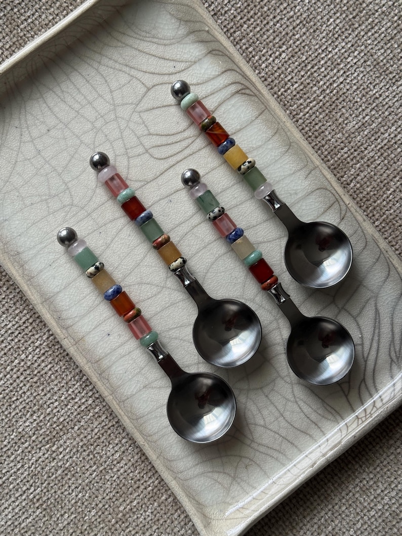 May include: Three silver-toned metal spoons with handles decorated with a series of multi-colored, cylindrical stone beads in shades of pink, green, blue, orange, and white, topped with a small silver-toned metal sphere at the end of each handle.