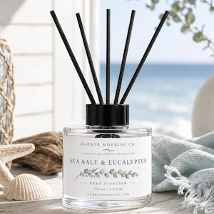 Könnte beinhalten: Ein durchsichtiger Glas-Diffusor mit schwarzem Verschluss und fünf schwarzen Stäbchen. Das weiße Etikett trägt die Aufschrift Harbor Morning Co. Coastal Wellness Collection Sea Salt & Eucalyptus Reed Diffuser 100 ml.
