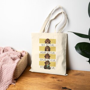 May include: A cream-coloured tote bag displaying four panels with monkey illustrations and the phrases "See No Evil," "Hear No Evil," "Speak No Evil," and "Pose No Evil." The bag has long handles.
